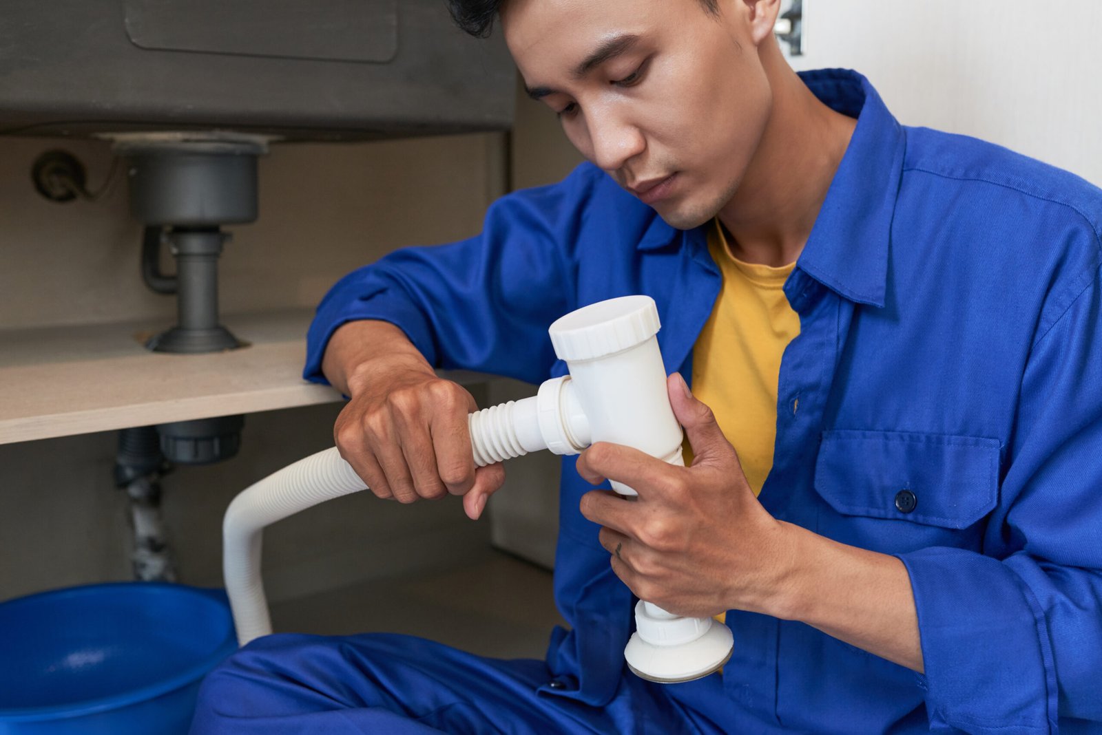 Young professional plumber concentrated on assembling sink pipe